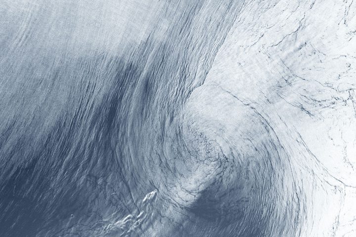 Thin layer of white clouds swirl above a blue background