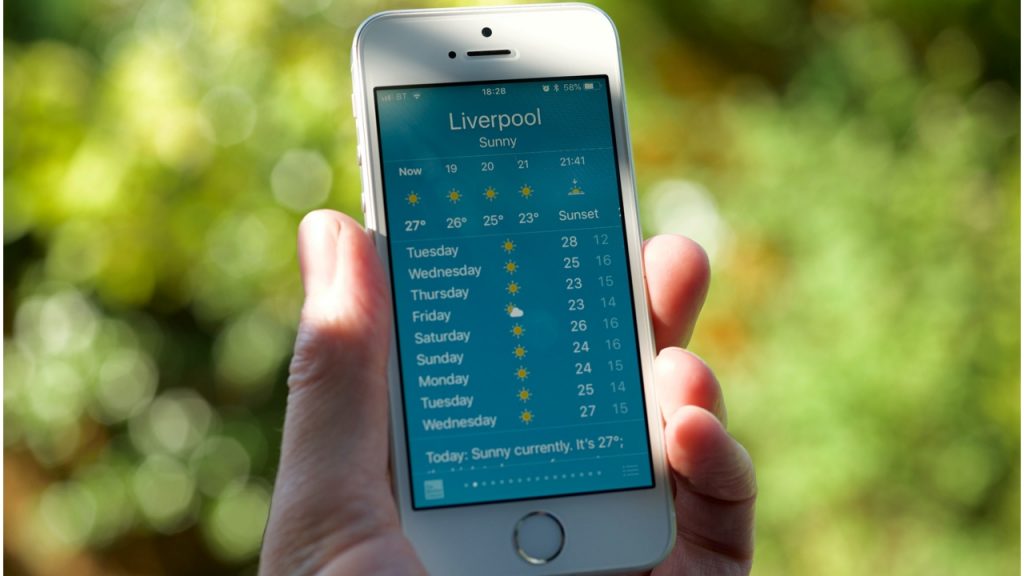 Hand holding a white iPhone displaying a weather forecast