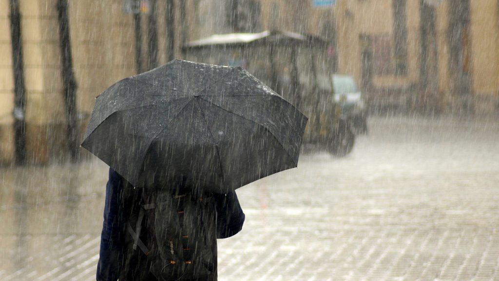 Person holds black umbrella in heavy rain