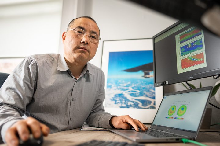 Person wearing grey shirt sits at desk with graphs displayed on two computer screens