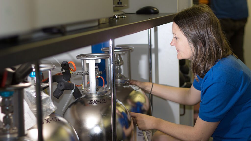 Person crouches and holds large gas cylinder in a laboratory