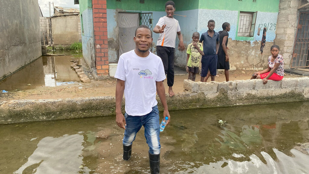A person wearing wellies stands in floodwater in a residential area in Africa