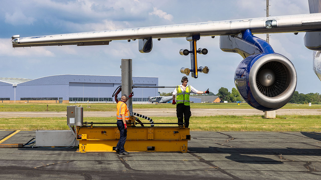2 people stand underneath the wing of an aircraft setting up a scientific instrument.